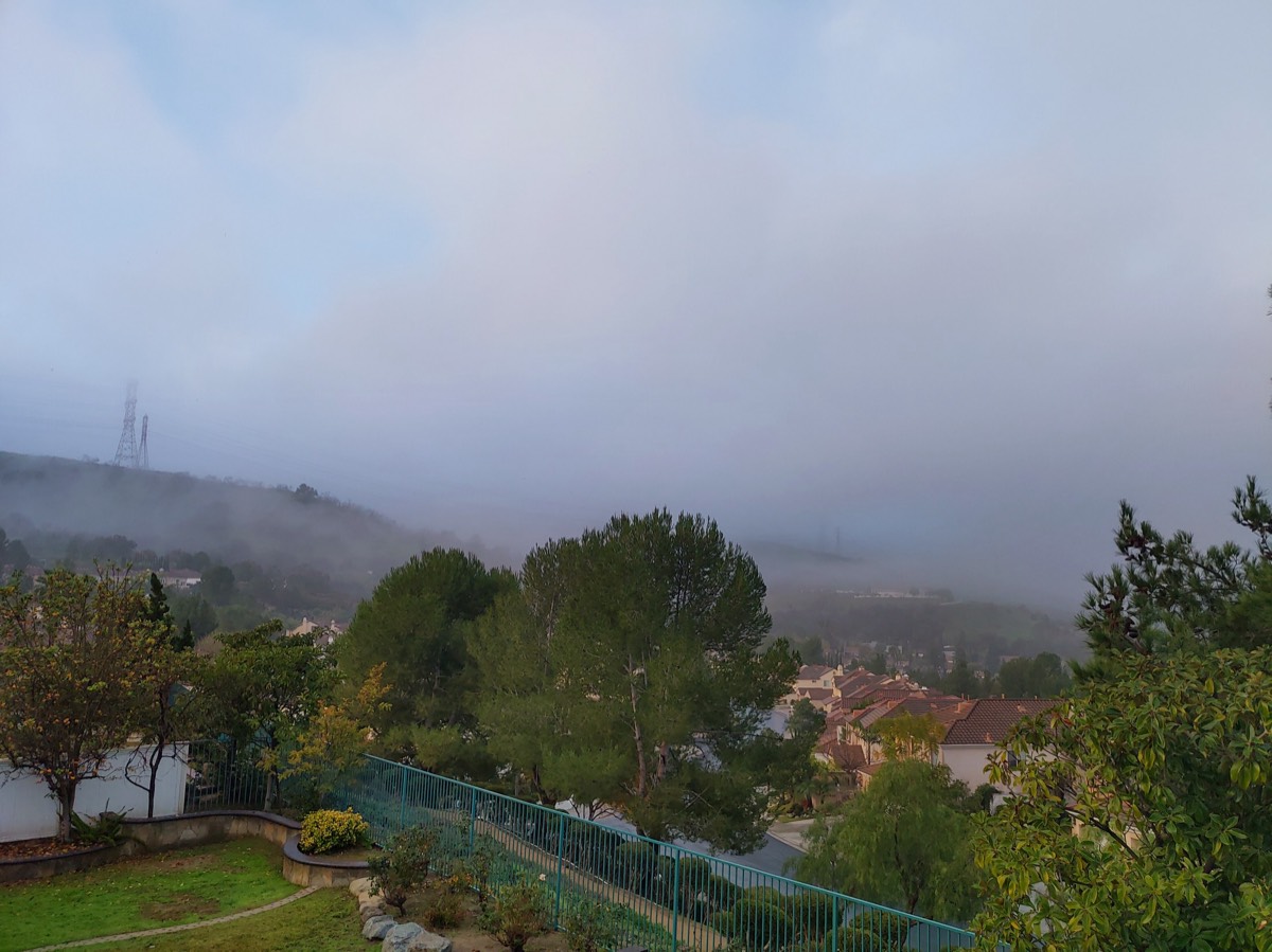 清晨浓雾笼罩的山坡住宅区,高压铁塔与屋顶在雾中若隐若现