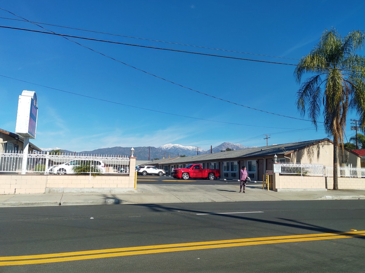 汽车旅馆街景,红色皮卡停在门前,棕榈树与远处雪山