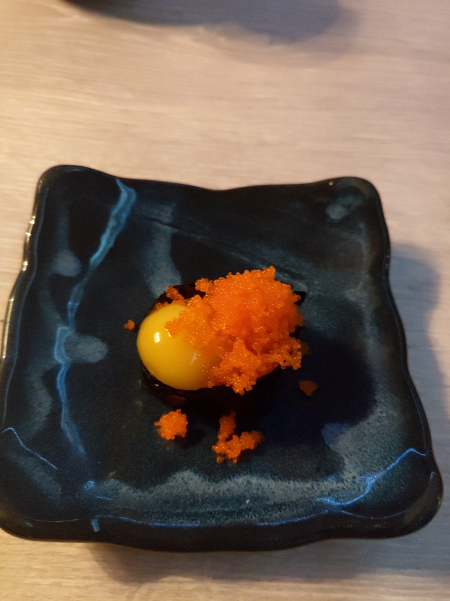 黑陶盘中一枚金黄生蛋黄,堆叠橙红鱼籽,黑色画板衬出撞色
