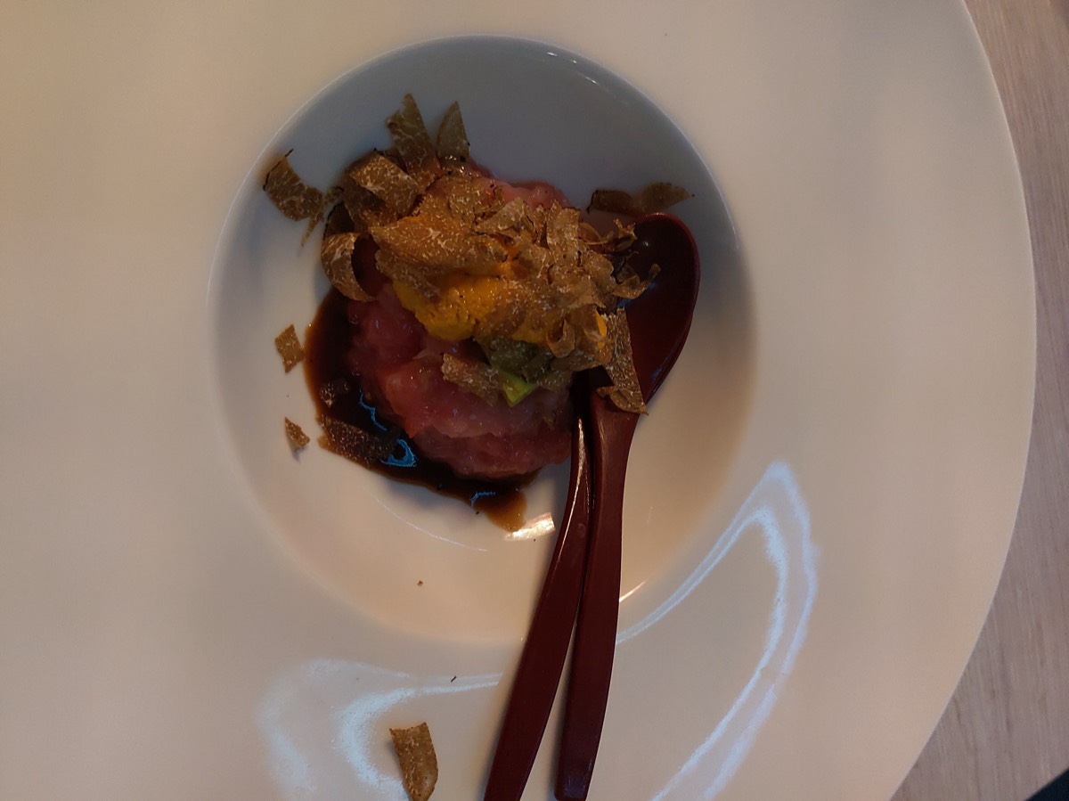 白色深盘中的生牛肉塔塔,铺满松露薄片,中央一枚蛋黄,木质勺筷斜放