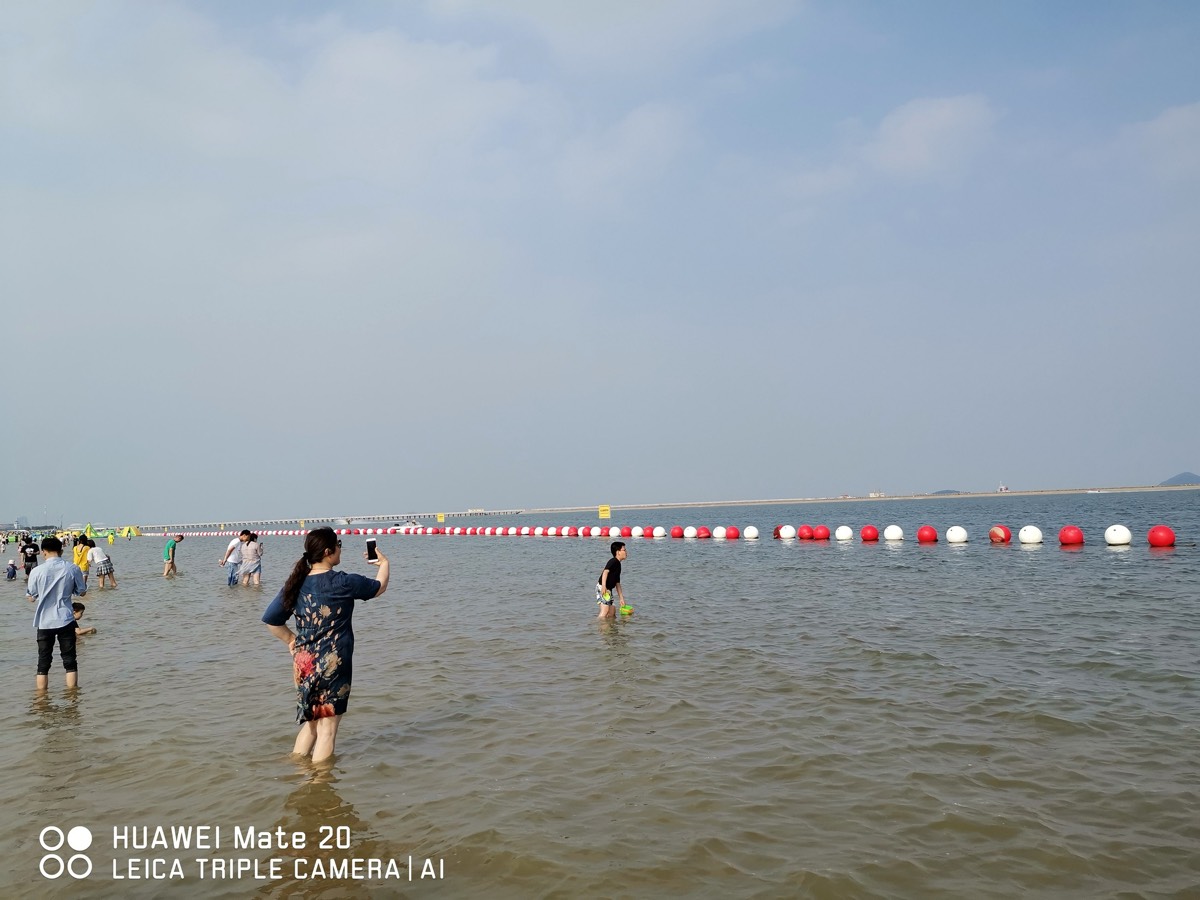 开阔浅海与延伸的红白浮标,家人举手机拍照