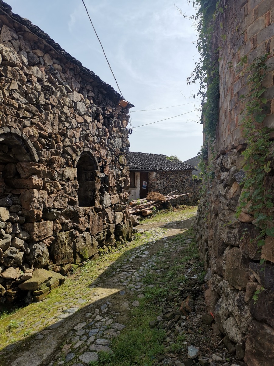 鹅卵石铺成的石村巷道,两侧石墙爬满藤蔓,尽头是石屋与天光